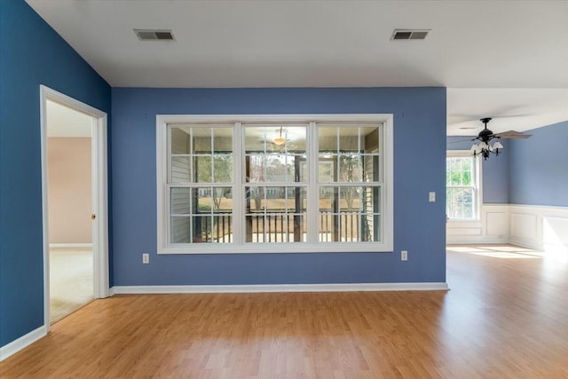 spare room featuring ceiling fan, visible vents, wood finished floors, and wainscoting