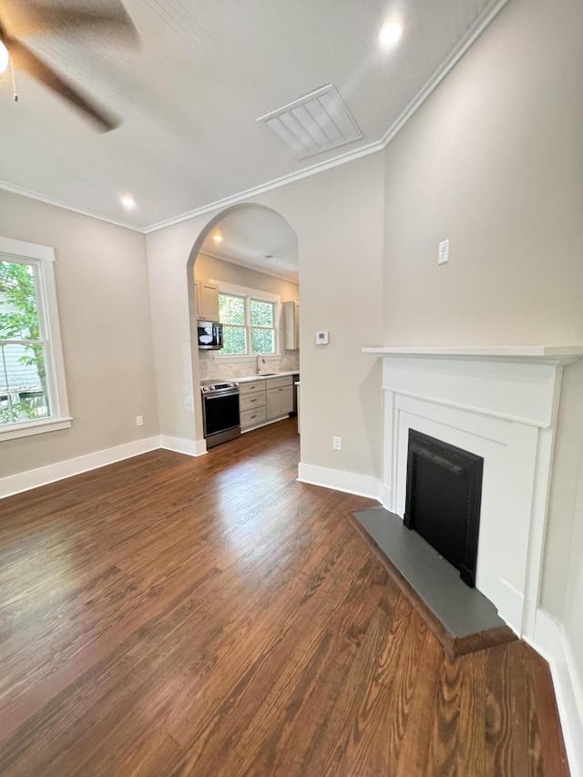 unfurnished living room with crown molding, a ceiling fan, dark wood-style floors, and a fireplace