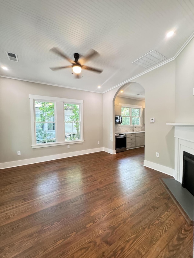unfurnished living room with crown molding, arched walkways, a ceiling fan, and visible vents