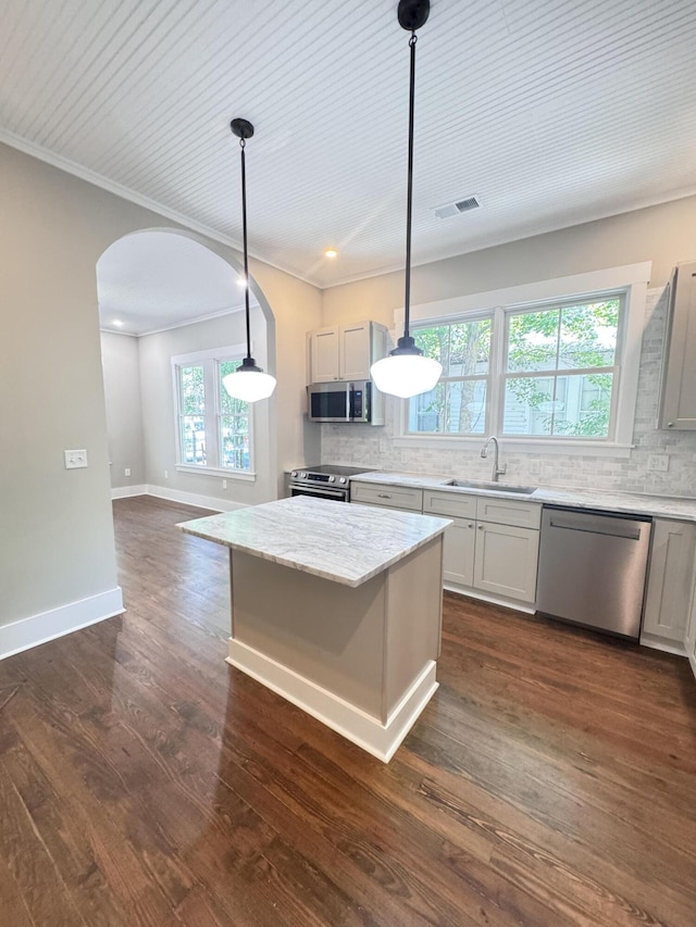 kitchen featuring stainless steel appliances, arched walkways, decorative backsplash, and a sink