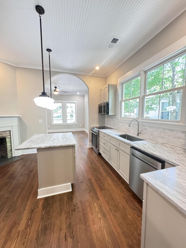 kitchen with a kitchen island, appliances with stainless steel finishes, tasteful backsplash, a sink, and light stone counters