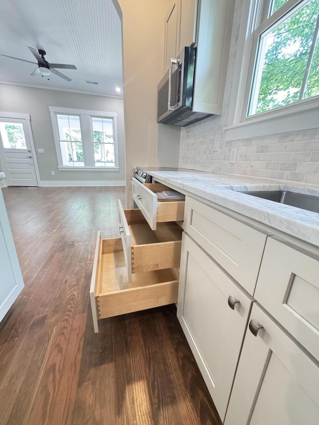 kitchen with ceiling fan, light stone counters, stainless steel microwave, backsplash, and dark wood-style floors