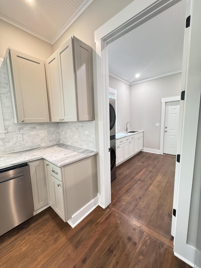 kitchen with stainless steel dishwasher, ornamental molding, stacked washer / drying machine, dark wood-style floors, and backsplash