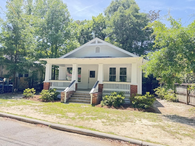 bungalow-style house with fence, covered porch, and brick siding