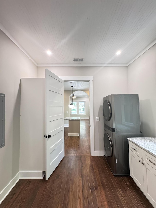 laundry area with baseboards, stacked washer and clothes dryer, cabinet space, and dark wood-type flooring