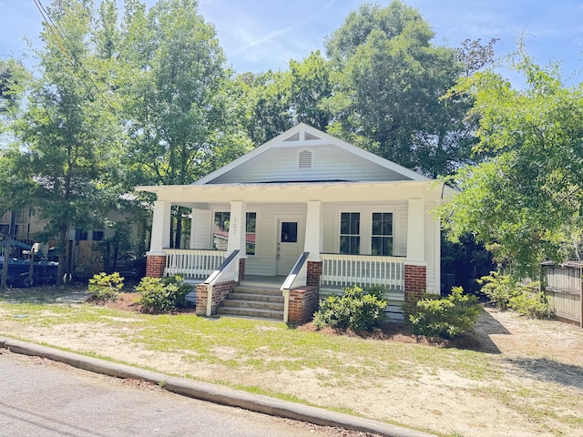 bungalow-style home with brick siding, fence, and covered porch