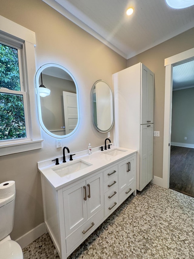 bathroom featuring baseboards, a sink, double vanity, and toilet