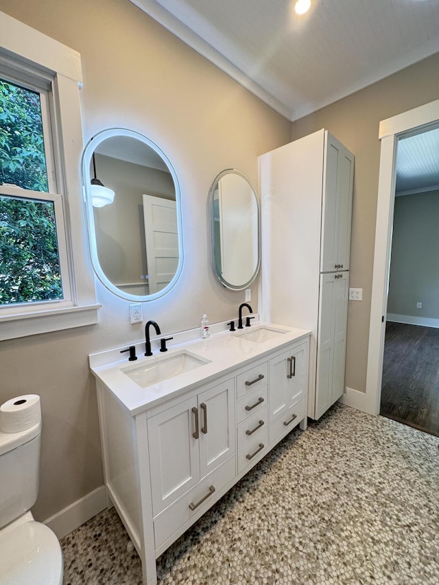 full bath featuring toilet, double vanity, baseboards, and a sink