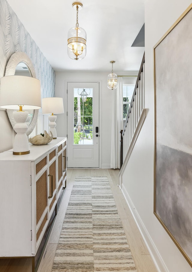 doorway to outside featuring a chandelier, baseboards, stairway, light wood-type flooring, and wallpapered walls