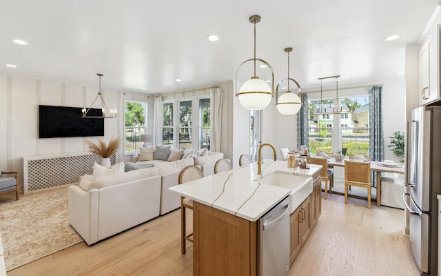 kitchen with light wood finished floors, open floor plan, stainless steel appliances, a kitchen bar, and a sink