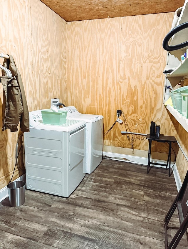 clothes washing area with dark wood-type flooring, washer and clothes dryer, and wood walls