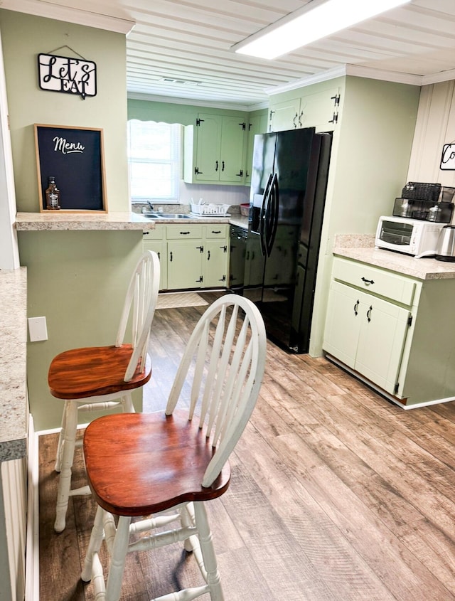 kitchen with black appliances, ornamental molding, light hardwood / wood-style floors, and green cabinetry