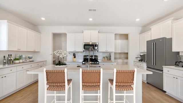 kitchen with visible vents, an island with sink, a sink, stainless steel appliances, and light wood-style floors