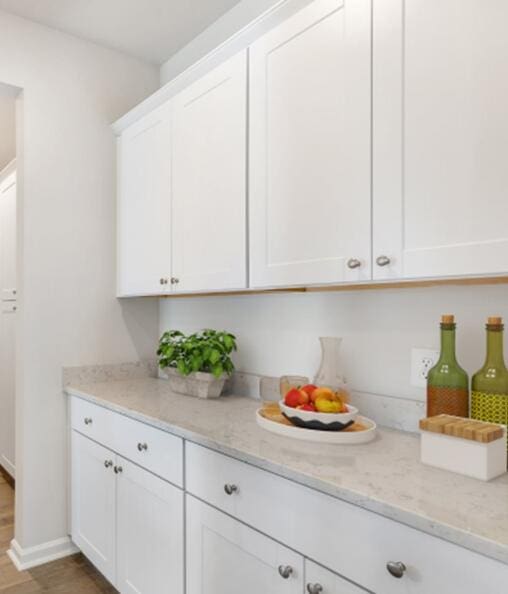 kitchen with baseboards, light stone countertops, wood finished floors, and white cabinetry