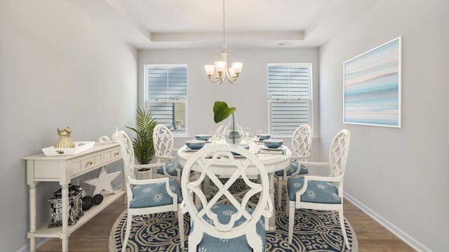 dining space with an inviting chandelier, a raised ceiling, wood finished floors, and baseboards