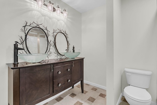 bathroom featuring toilet, double vanity, baseboards, and a sink