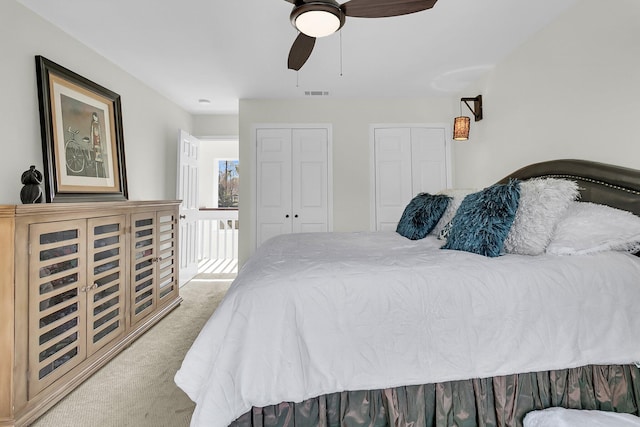 bedroom featuring multiple closets, light colored carpet, ceiling fan, and visible vents