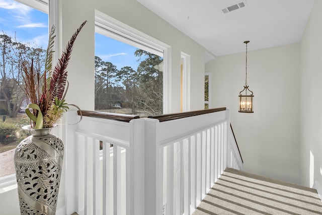 hallway featuring visible vents, a notable chandelier, and an upstairs landing