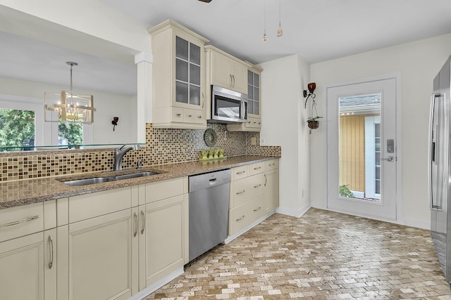 kitchen featuring cream cabinetry, stainless steel appliances, tasteful backsplash, glass insert cabinets, and a sink