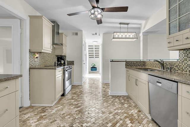 kitchen with cream cabinets, stainless steel appliances, a sink, wall chimney exhaust hood, and glass insert cabinets