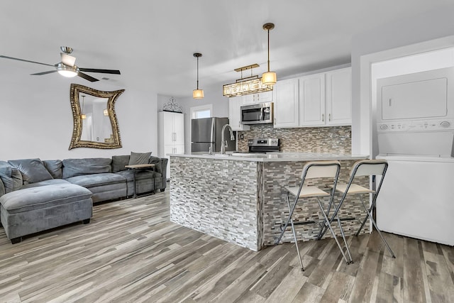 kitchen with stainless steel appliances, a peninsula, white cabinetry, stacked washer / drying machine, and light countertops