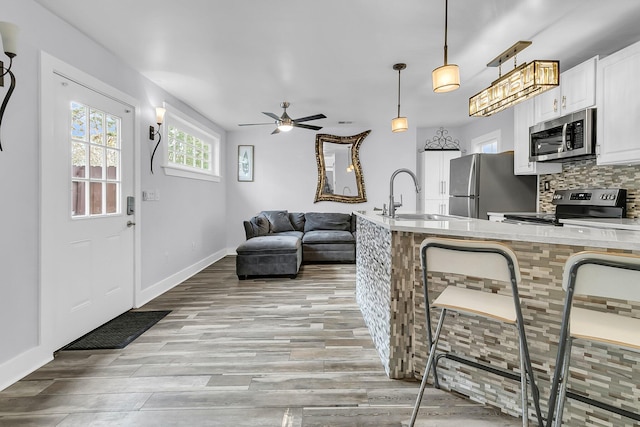 kitchen with stainless steel appliances, a sink, white cabinets, hanging light fixtures, and light countertops