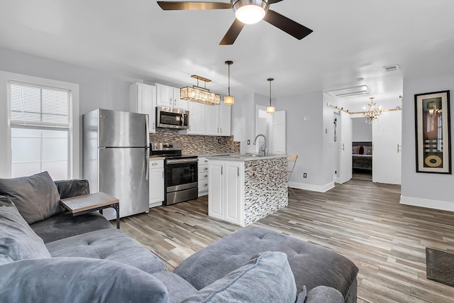 kitchen with stainless steel appliances, white cabinets, open floor plan, hanging light fixtures, and an island with sink