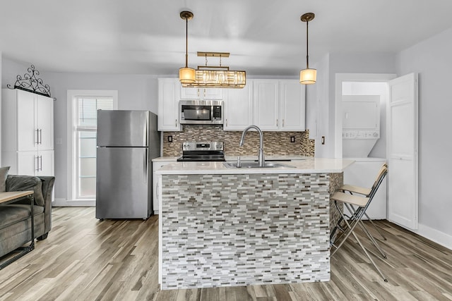 kitchen with stacked washer and clothes dryer, light countertops, appliances with stainless steel finishes, white cabinets, and a sink