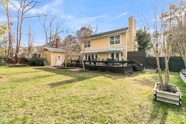 back of house with a chimney, stucco siding, a lawn, a fenced backyard, and a wooden deck