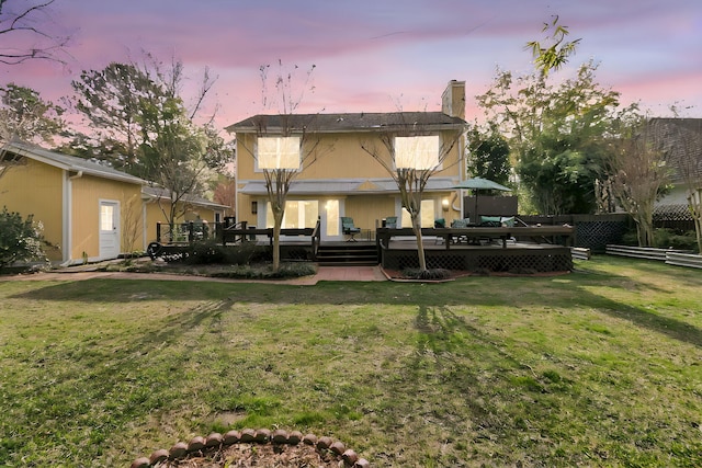 back of property at dusk with a yard, a chimney, a wooden deck, and fence