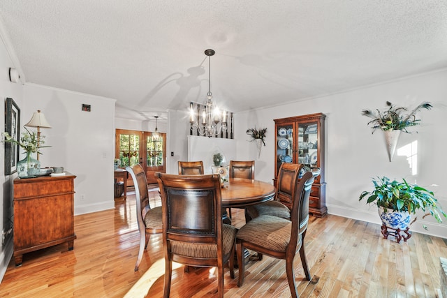 dining area featuring french doors, a notable chandelier, a textured ceiling, ornamental molding, and light wood-type flooring