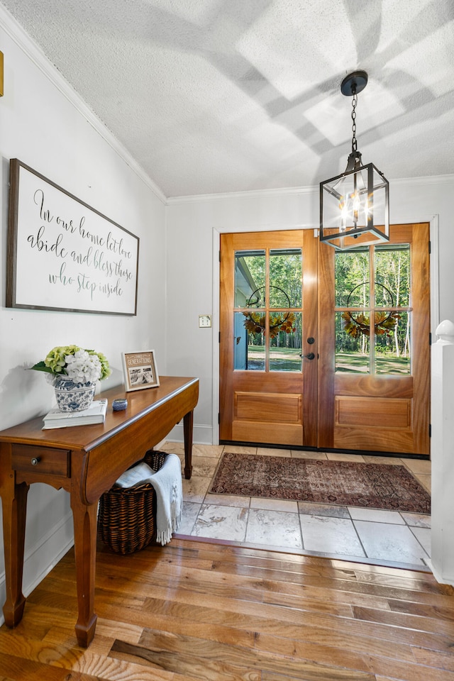 entryway featuring wood-type flooring, a textured ceiling, an inviting chandelier, and ornamental molding