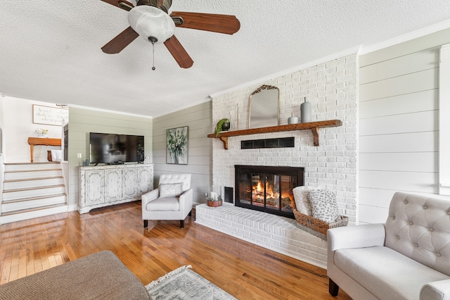 living room featuring a textured ceiling, hardwood / wood-style flooring, ceiling fan, and a fireplace