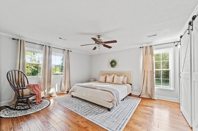 bedroom with multiple windows, a barn door, ceiling fan, and light wood-type flooring