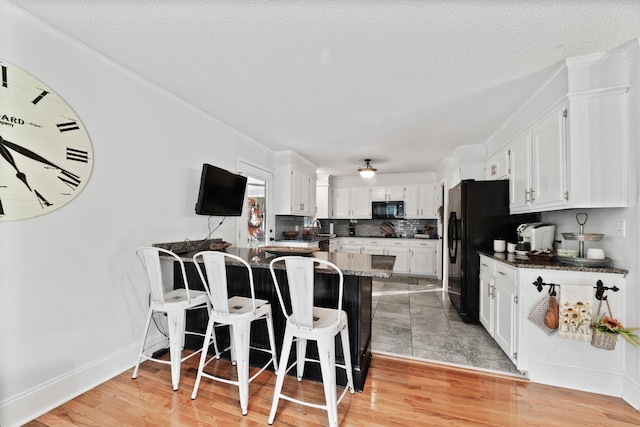 kitchen with kitchen peninsula, a textured ceiling, a kitchen breakfast bar, white cabinetry, and light wood-type flooring