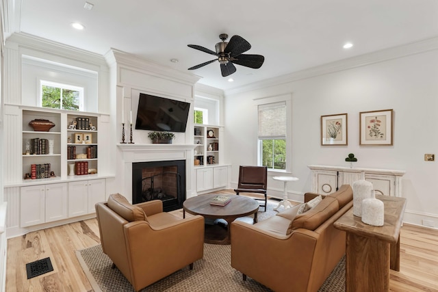 living area with ornamental molding, a fireplace, light wood-type flooring, ceiling fan, and plenty of natural light