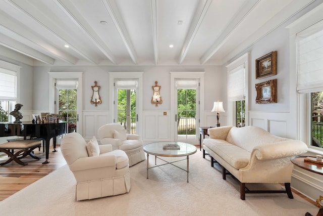 living area featuring a decorative wall, beam ceiling, healthy amount of natural light, wood finished floors, and wainscoting