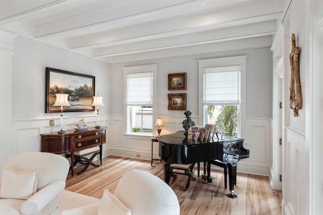 sitting room with light wood-style flooring, a decorative wall, beam ceiling, and a wainscoted wall