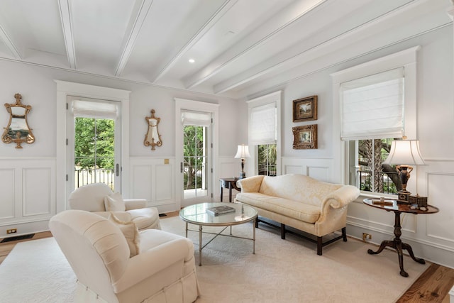 living area featuring a decorative wall, beam ceiling, and wainscoting