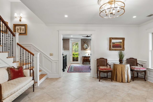 foyer featuring a decorative wall, stairs, crown molding, a chandelier, and a wainscoted wall