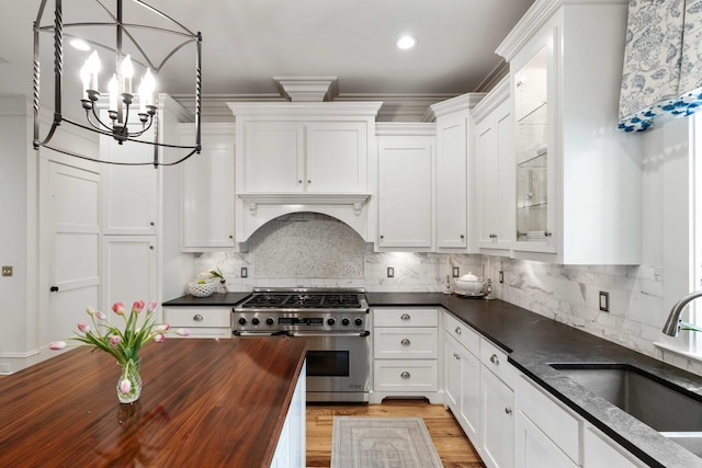 kitchen featuring stainless steel stove, butcher block counters, a sink, white cabinets, and a chandelier