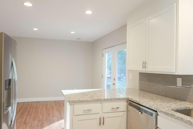 kitchen featuring a peninsula, white cabinets, light wood-style floors, appliances with stainless steel finishes, and tasteful backsplash