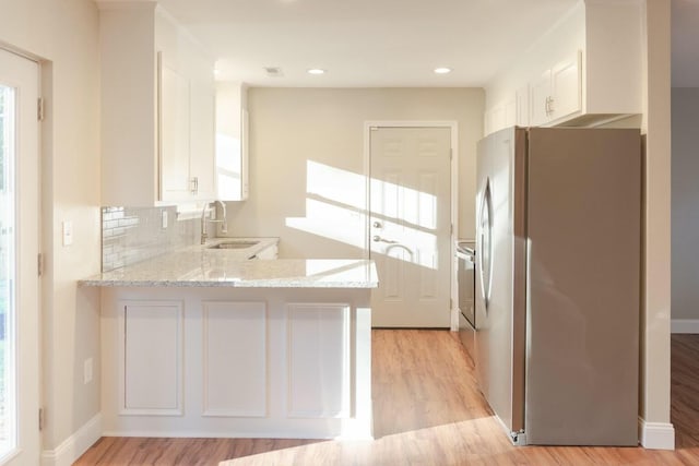 kitchen with light stone countertops, a peninsula, freestanding refrigerator, a sink, and white cabinets