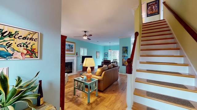 stairway with ceiling fan, a fireplace, wood finished floors, and baseboards