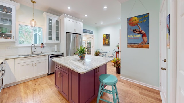 kitchen featuring light wood finished floors, decorative backsplash, appliances with stainless steel finishes, light stone countertops, and a sink