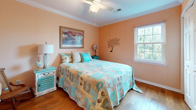 bedroom featuring wood finished floors, a ceiling fan, baseboards, visible vents, and crown molding