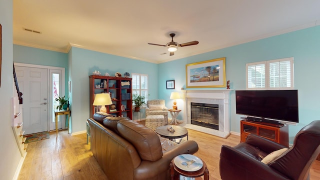 living area with baseboards, visible vents, a glass covered fireplace, crown molding, and light wood-style floors