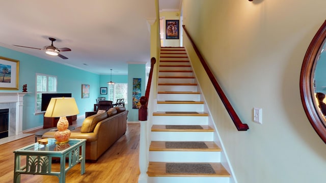 stairway with a ceiling fan, wood finished floors, ornamental molding, and a premium fireplace