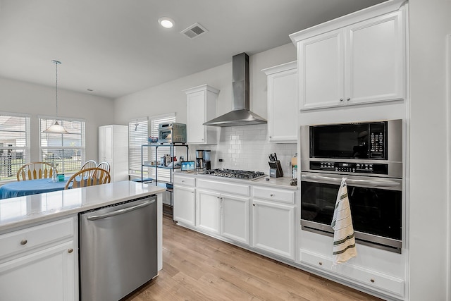 kitchen featuring light wood-style floors, stainless steel appliances, backsplash, wall chimney exhaust hood, and visible vents