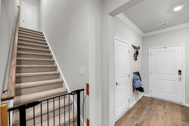 stairs featuring baseboards, wood finished floors, visible vents, and crown molding